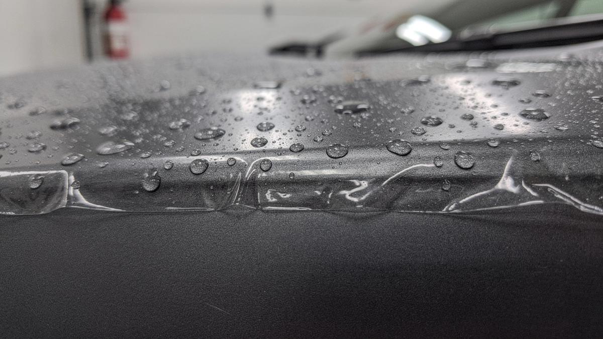 Macro view of a paint protection film edge on a dark car panel with a paint depth gauge callout